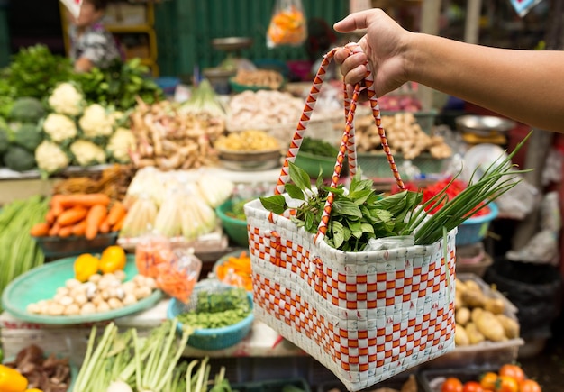 Main tenant un panier avec des légumes sur le marché humide