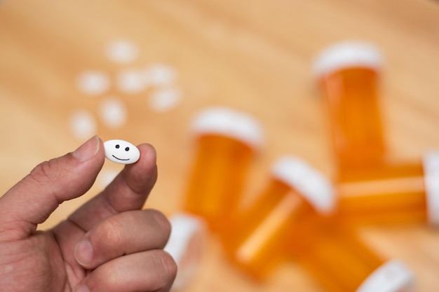 Main tenant une pilule avec un visage heureux dessiné et des pilules et des bouteilles vides en arrière-plan avec espace de copie