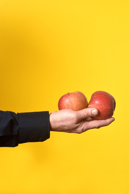 Main tenant une pomme deux sur fond jaune