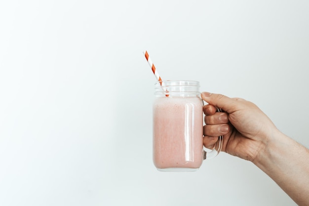 une main tenant un pot de smoothie à la fraise sur un fond blanc