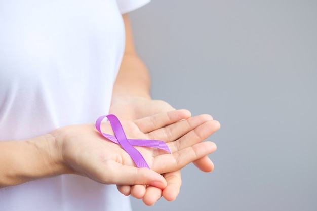 Main tenant un ruban violet pour le cancer du pancréas, de l'œsophage, des testicules, le monde d'Alzheimer, l'épilepsie, le lupus, la sarcoïdose, la fibromyalgie et le mois de sensibilisation à la violence domestique. Concept de la journée mondiale du cancer