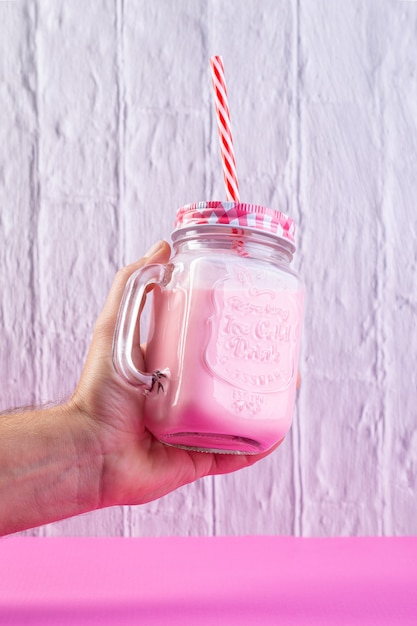 Main tenant le shake aux fraises sur fond rose et.