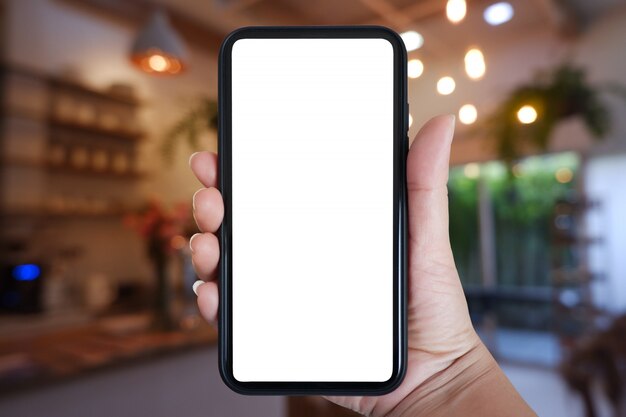 Photo main tenant le smartphone avec écran blanc pour l'application à l'intérieur du café