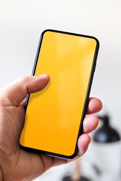 Main tenant un smartphone avec fond de bureau écran jaune blanc