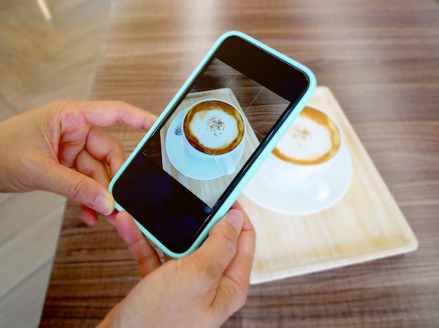 Main tenant le smartphone et prendre une photo d'un cappuccino