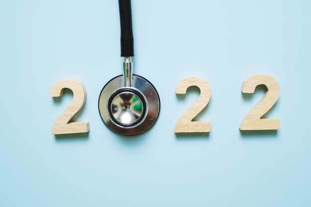 Main tenant le stéthoscope avec numéro 2022 sur fond bleu. Bonne année pour les soins de santé, l'assurance, le bien-être et le concept médical