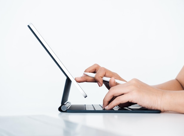 Main tenant un stylo électronique blanc ou un crayon touchant à l'écran sur l'écran de la tablette numérique en tapant sur l'ordinateur clavier isolé sur fond blanc avec vue latérale de l'espace de copie Travailler avec la technologie