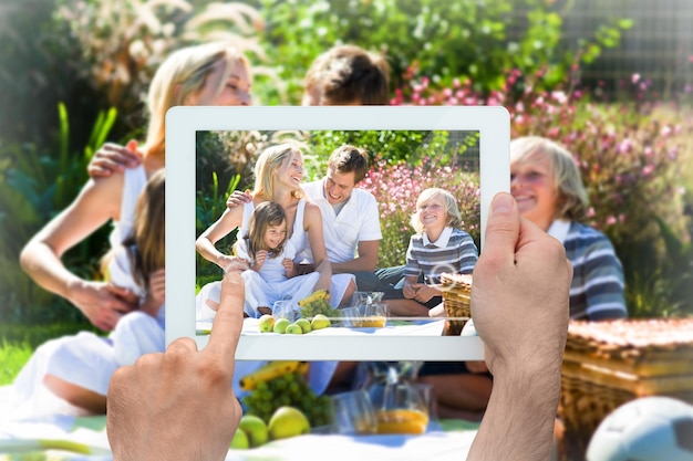Main tenant un tablet pc montrant une famille heureuse ayant un pique-nique