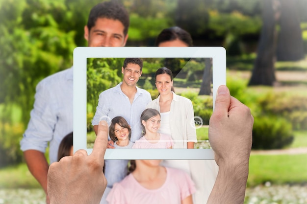 Photo main tenant une tablette pc montrant une famille souriant à la caméra dans le parc