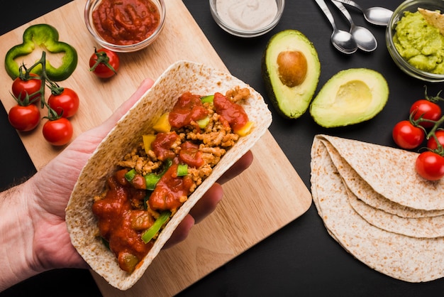 Main tenant un taco près d&#39;une planche à découper parmi des légumes et des sauces