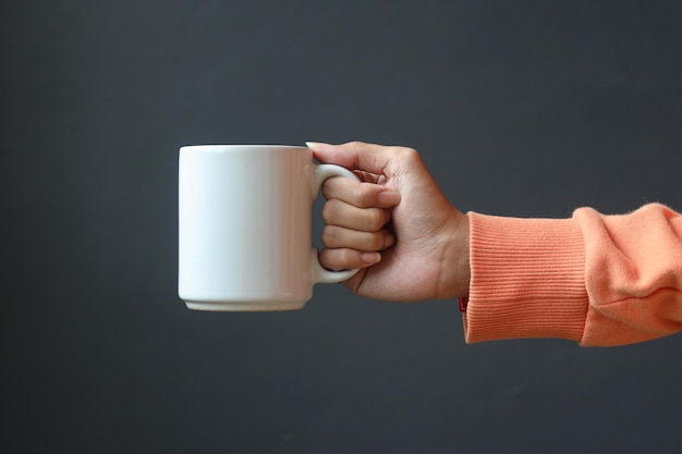 main tenant une tasse de café blanche isolée sur fond gris foncé maquette de tasse en porcelaine blanche