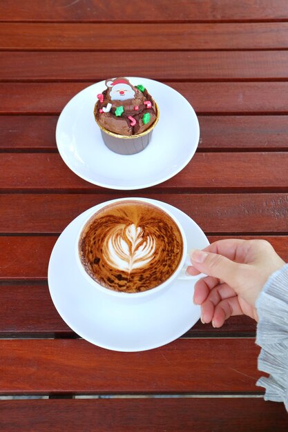 Main tenant une tasse de café cappuccino chaud avec une assiette de cupcake au chocolat de Noël
