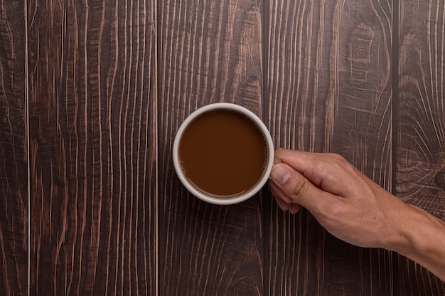 Main tenant une tasse de café sur un fond de bois