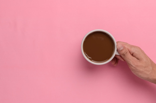 Main tenant une tasse de café sur fond rose