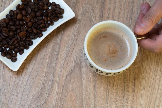 main tenant une tasse de café avec des grains de café d'un côté