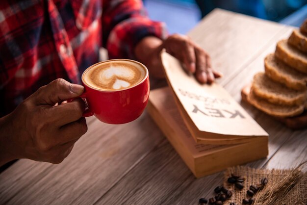 Main tenant une tasse de café et lisant une clé de livre de réussite - concept lifestyle