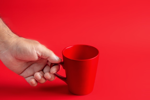 Main tenant une tasse de café rouge sur fond rouge