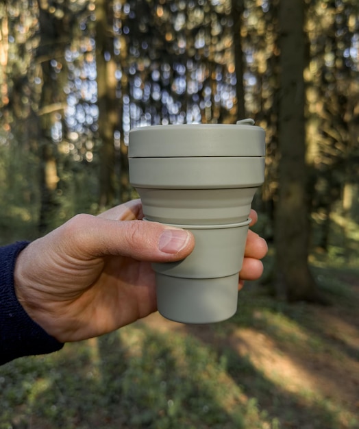 Photo main tenant une tasse de café tasse pliable en silicone dans la nature forestière ensoleillée eco et concept zéro déchet