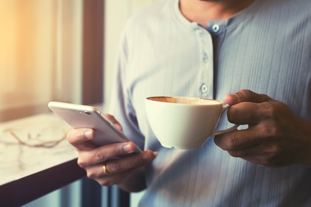 main tenant la tasse de café et en utilisant un téléphone intelligent