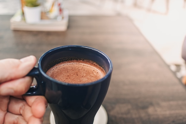 Main tenant une tasse de chocolat chaud dans un café