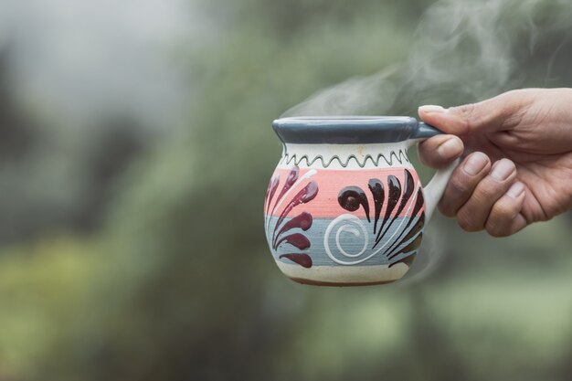 Main tenant une tasse faite à la main avec une boisson chaude dans la forêt