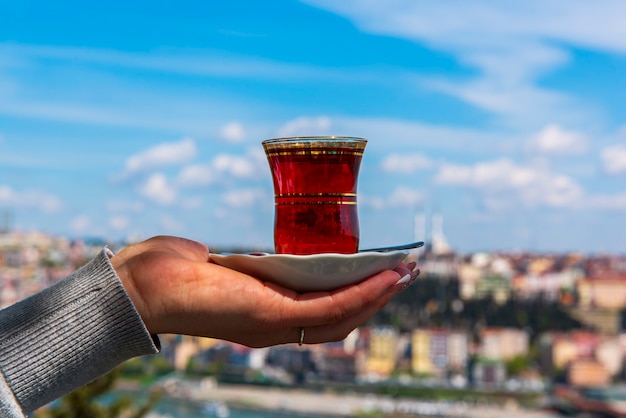 Main tenant une tasse de thé turc traditionnel contre la vue d'Istanbul, Turquie