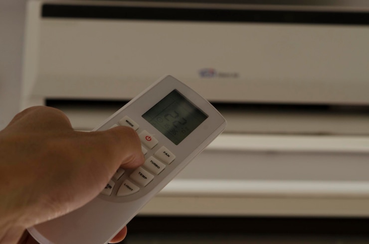 Photo la main tenant la télécommande du climatiseur avec le climatiseur en arrière-plan dans le département pour changer la température de la pièce