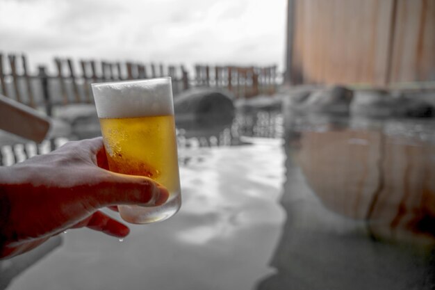 Une main tenant un verre de bière devant un bassin d'eau