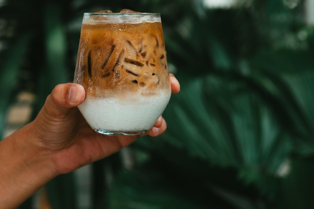 Main tenir le café au lait glacé dans un verre avec de la crème sur fond de boisson d'été froide en bas