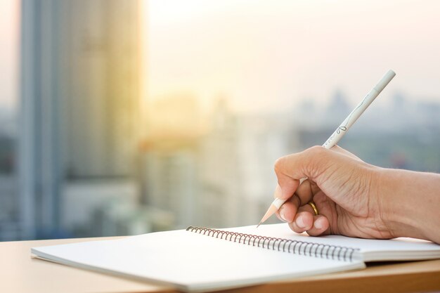 Main tenir le crayon écrit sur le carnet de notes avec le fond de coucher de soleil flou.