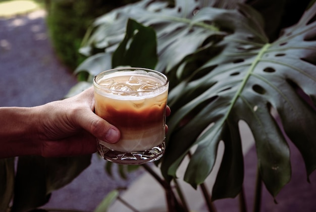 Main Tenir Du Café Au Lait Glacé Dans Un Grand Verre D'été Froid Avec Fond De Nature Verdoyante