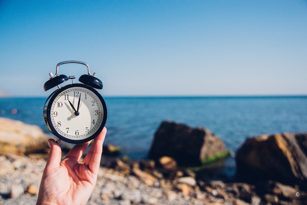 Main tenir la montre sur fond de plage. Réveil sur fond de mer et de sable à différentes heures avec les vacances d'été. Concept de temps de vacances.