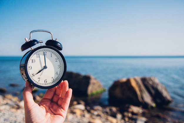 Main tenir la montre sur fond de plage. Réveil sur fond de mer et de sable à différentes heures avec les vacances d'été. Concept de temps de vacances.