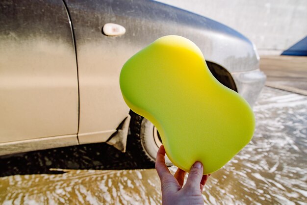 Main tenir la voiture sale éponge jaune sur le concept de lavage de voiture de fond
