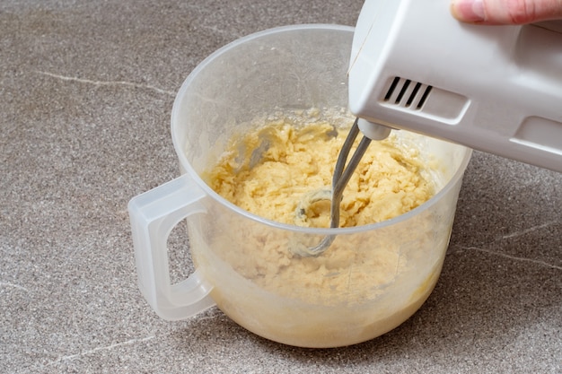 Une main tient un batteur pour battre la pâte dans un bol en plastique. Pétrir la pâte dans un mélangeur. Concept de cuisson maison.