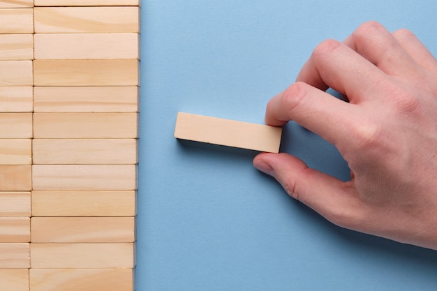 Main tient un bloc de bois sur un espace bleu.