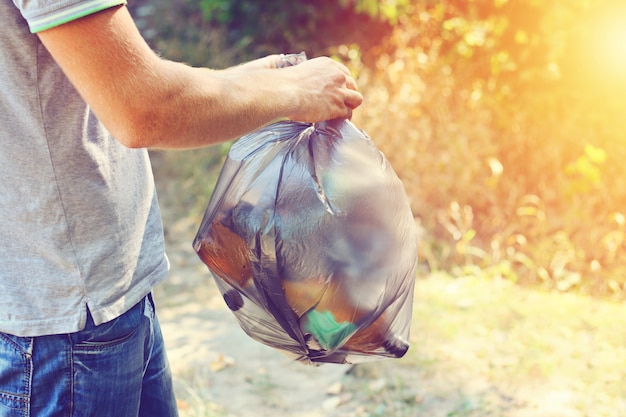 Main tient contre le sac en plastique noir pleine de déchets de forêt