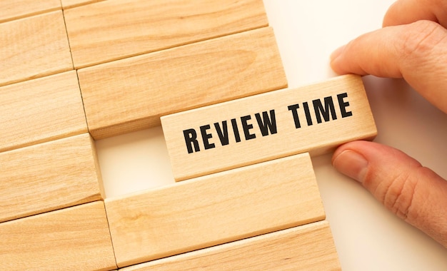 La main tient un cube en bois avec le texte REVIEW TIME