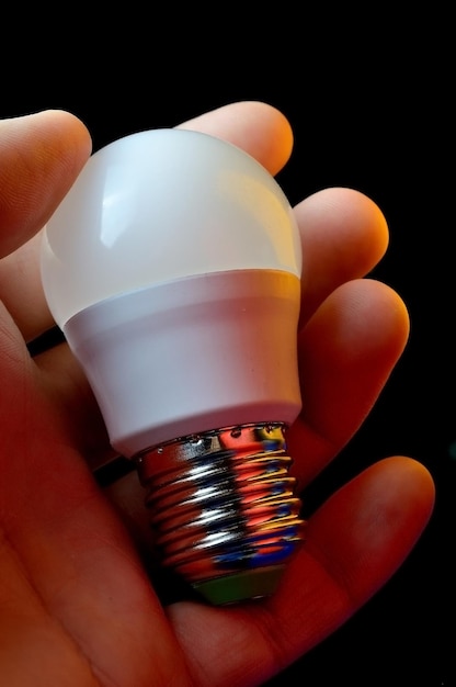 La main tient une lampe LED avec une base e14 illuminée de différentes couleurs.