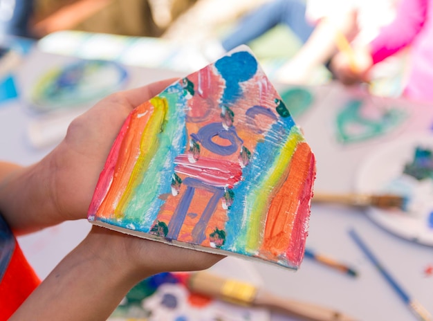 Une main tient une maison faite de peinture colorée.