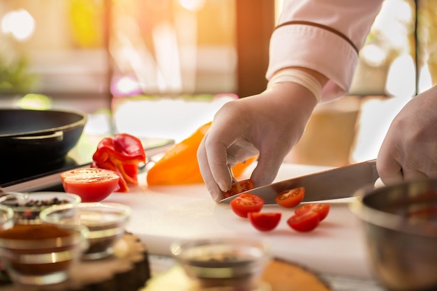 La main tient un morceau de tomate. Poivron rouge et jaune. Il est temps de préparer la soupe. Recevez des vitamines du repas.