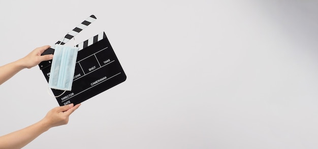 Photo la main tient un panneau de clapet ou une ardoise de film et un masque facial sur fond blanc. il utilise dans la production vidéo et le cinéma.