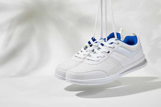 La main tient par des lacets baskets blanches Main tenir des chaussures de sport sur un fond blanc