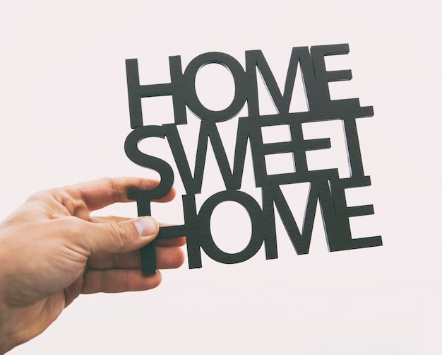 La main tient la phrase en bois Home sweet home Concept d'achat ou de construction d'une maison de rêves