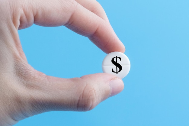 Une main tient une pilule médicale avec un signe de devise dollar sur fond bleu Le concept d'une hausse du prix des médicaments