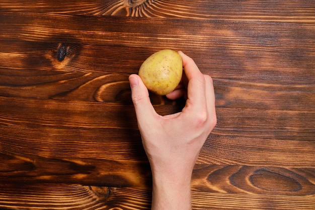 main tient la pomme de terre sur le bois brûlé. Vue de dessus.