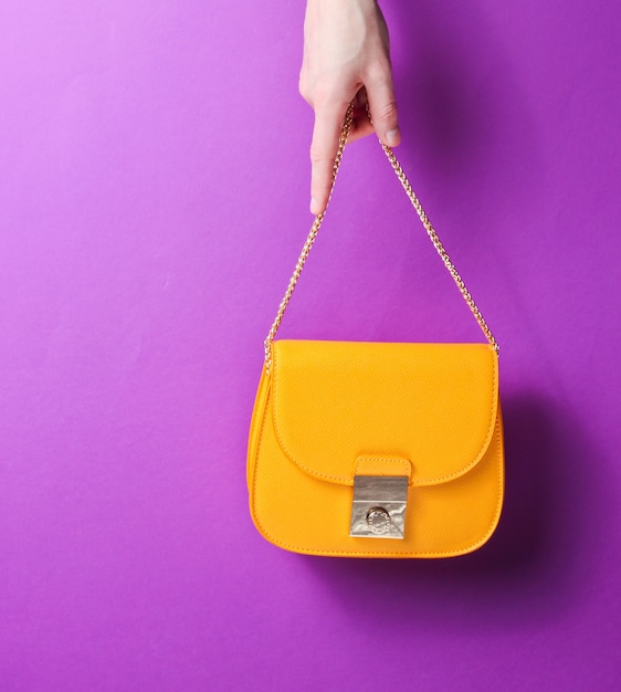 Main tient un sac en cuir jaune à la mode avec une chaîne dorée