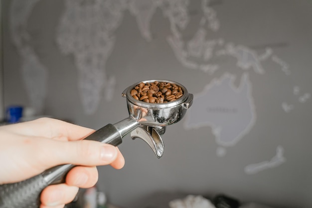 Une main tient un support rempli de grains de café dans le contexte d'une carte du monde