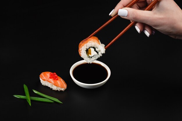 La main tient des sushis sur un bol avec de la sauce soja sur un tableau noir.