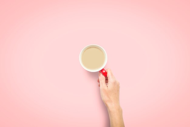 Une main tient une tasse de café chaud sur fond rose. Concept de petit déjeuner avec café ou thé. Bonjour, nuit, insomnie. Mise à plat, vue de dessus